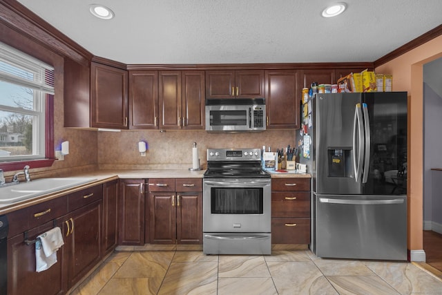 kitchen with tasteful backsplash, appliances with stainless steel finishes, ornamental molding, light countertops, and a sink