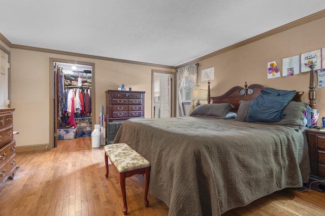 bedroom with light wood finished floors, baseboards, ornamental molding, a spacious closet, and a closet