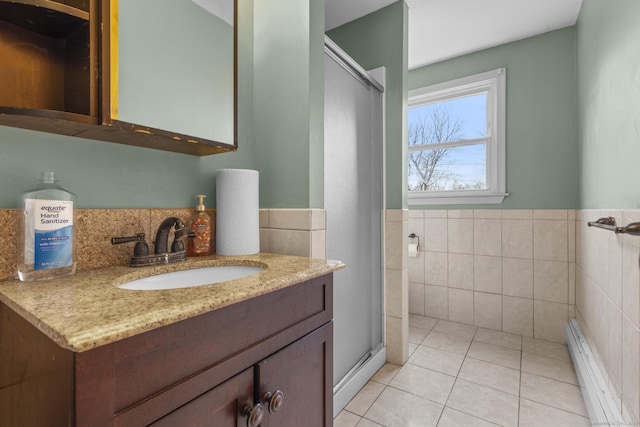 bathroom featuring tile patterned flooring, baseboard heating, vanity, a shower stall, and tile walls