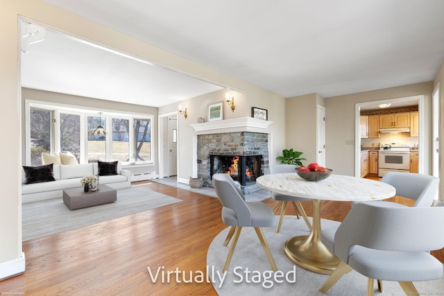 dining space with a baseboard radiator, baseboards, light wood-style floors, and a fireplace