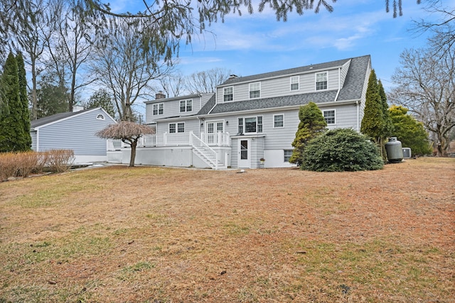 rear view of house featuring roof with shingles, a lawn, a chimney, and a wooden deck