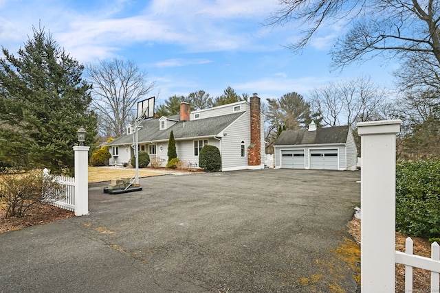 view of property exterior featuring aphalt driveway, an outbuilding, fence, and a chimney