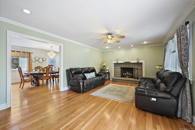 living room featuring ornamental molding, light wood-type flooring, ceiling fan, and a stone fireplace