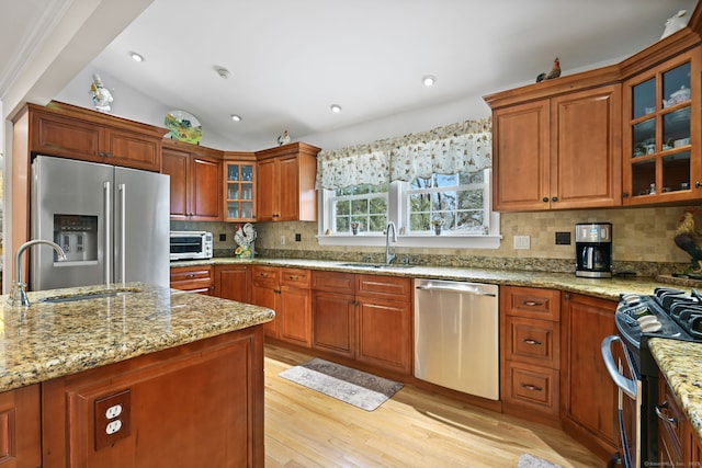 kitchen with stainless steel appliances, a sink, light wood-style flooring, and tasteful backsplash