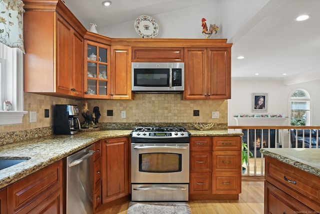 kitchen featuring decorative backsplash, light wood-style flooring, glass insert cabinets, appliances with stainless steel finishes, and light stone counters