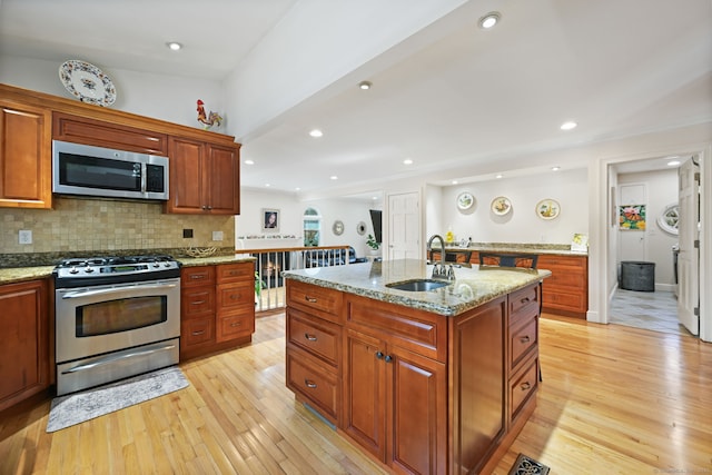 kitchen with stainless steel appliances, a sink, backsplash, and light wood finished floors