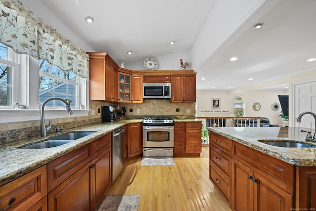 kitchen with stainless steel appliances, a sink, light wood-style flooring, and light stone countertops