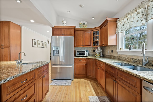 kitchen featuring stainless steel appliances, brown cabinets, a sink, and light stone countertops