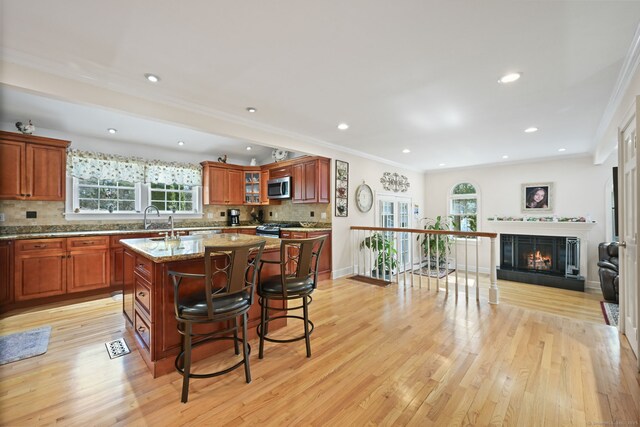 kitchen featuring a center island with sink, a breakfast bar area, tasteful backsplash, stainless steel microwave, and light wood-type flooring