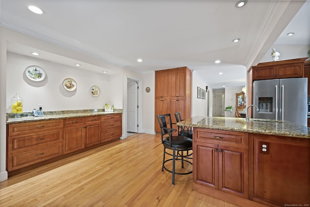 kitchen with a breakfast bar, crown molding, light wood finished floors, a sink, and stainless steel fridge