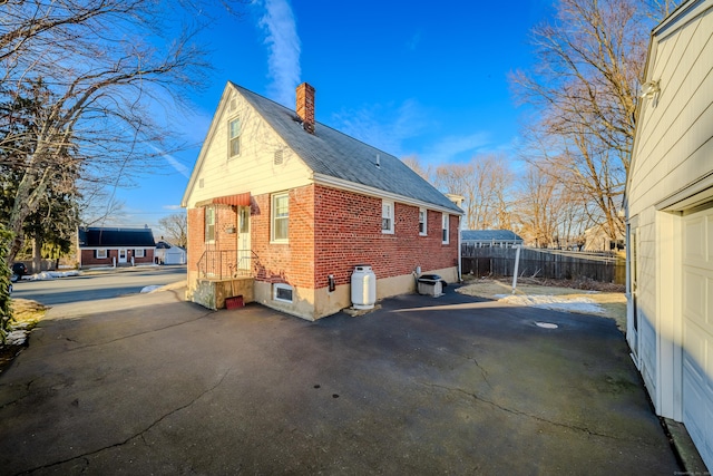 view of home's exterior featuring cooling unit, brick siding, fence, and a chimney