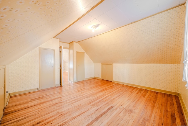 additional living space featuring wallpapered walls, baseboards, vaulted ceiling, and hardwood / wood-style floors