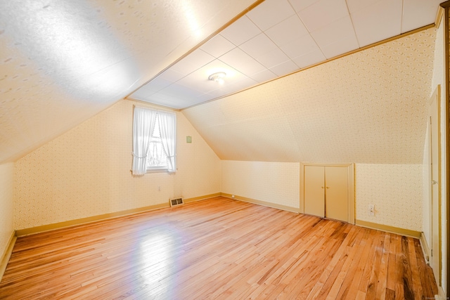 additional living space with wallpapered walls, baseboards, visible vents, lofted ceiling, and light wood-style floors