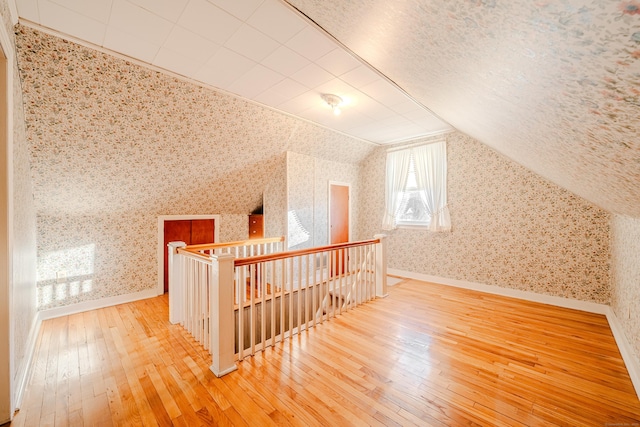 bonus room featuring lofted ceiling, wood-type flooring, a textured ceiling, baseboards, and wallpapered walls