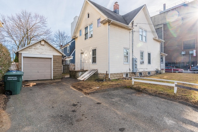 view of side of home featuring a chimney, a detached garage, fence, and an outdoor structure