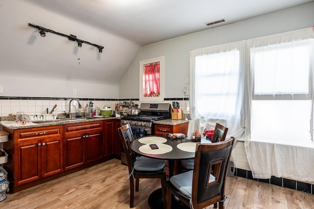 kitchen featuring light stone counters, lofted ceiling, light wood-style flooring, a sink, and stainless steel gas range