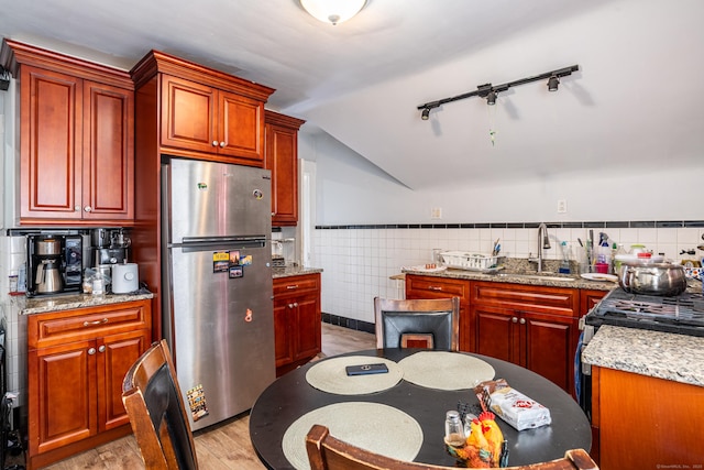 kitchen featuring lofted ceiling, a wainscoted wall, a sink, light wood-style floors, and appliances with stainless steel finishes