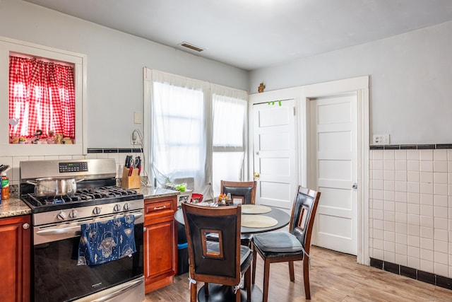 kitchen with light wood-style flooring, visible vents, tile walls, brown cabinetry, and gas range