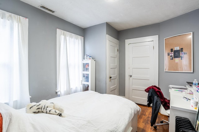 bedroom with dark wood-style floors, visible vents, and a textured ceiling