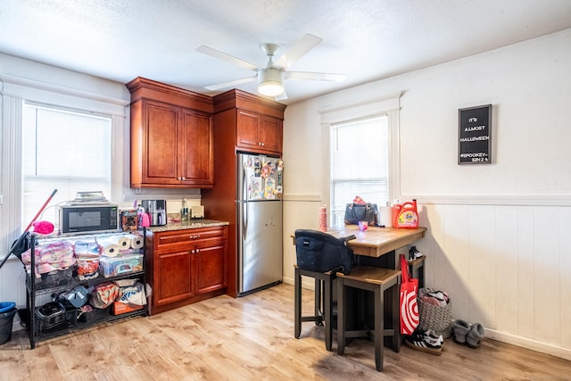 kitchen featuring light wood-style flooring, brown cabinetry, freestanding refrigerator, ceiling fan, and black microwave