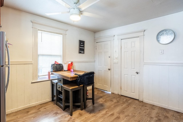 dining space featuring a ceiling fan, a wainscoted wall, and light wood finished floors