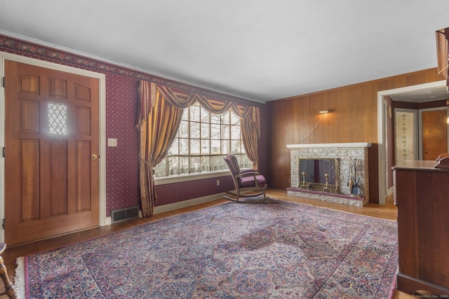 interior space with a stone fireplace, wood finished floors, visible vents, and wallpapered walls