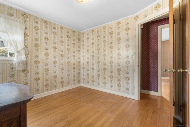 spare room with wallpapered walls, baseboards, and wood finished floors