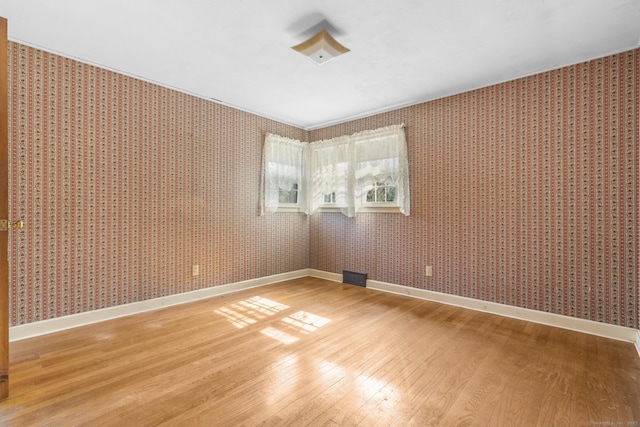 empty room with baseboards, light wood finished floors, and wallpapered walls