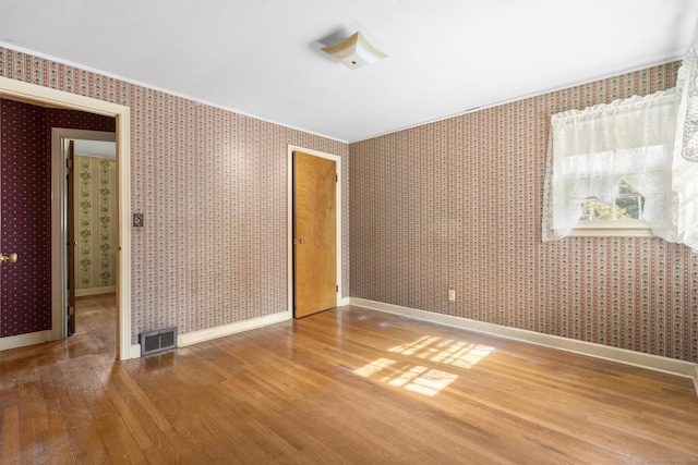 unfurnished room with wood finished floors, visible vents, baseboards, and wallpapered walls