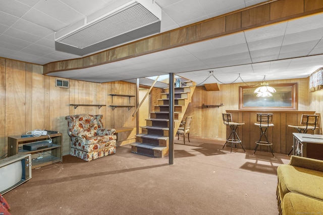 finished basement with stairway, wooden walls, visible vents, and carpet flooring