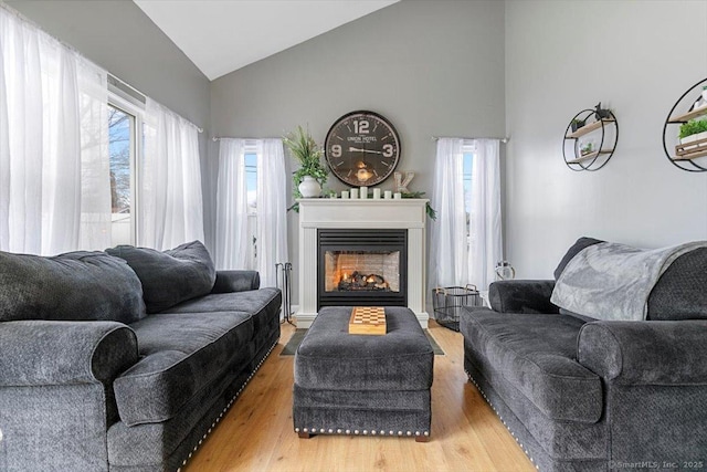 living room featuring vaulted ceiling, a warm lit fireplace, and wood finished floors