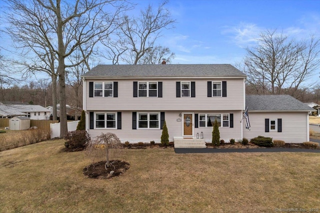 colonial house with an outbuilding, roof with shingles, a chimney, a front yard, and fence