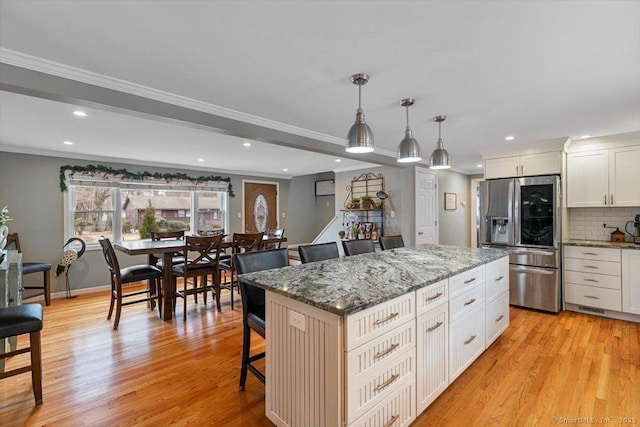 kitchen with light wood-style flooring, a breakfast bar, decorative backsplash, a center island, and stainless steel fridge