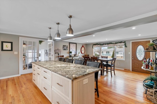 kitchen with a breakfast bar area, a kitchen island, french doors, light wood-type flooring, and crown molding