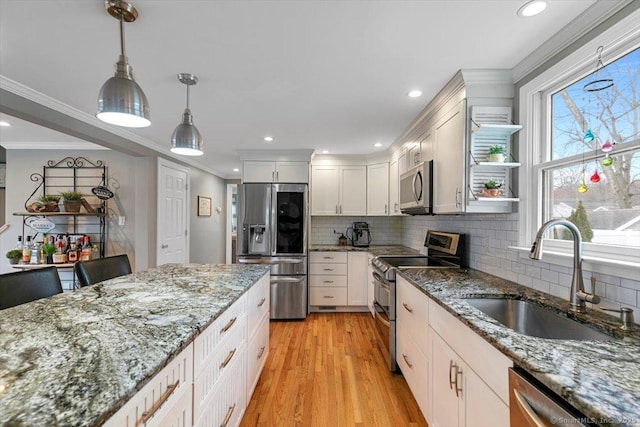 kitchen with pendant lighting, stainless steel appliances, ornamental molding, a sink, and light wood-type flooring