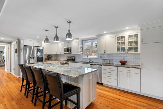 kitchen featuring light wood finished floors, tasteful backsplash, a kitchen breakfast bar, stainless steel appliances, and a sink