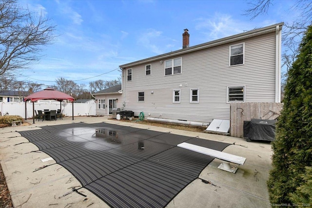 rear view of property featuring a chimney, fence, a gazebo, a patio area, and outdoor dining space