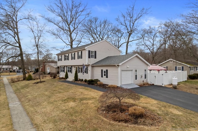 colonial house featuring aphalt driveway, a garage, fence, roof with shingles, and a front yard