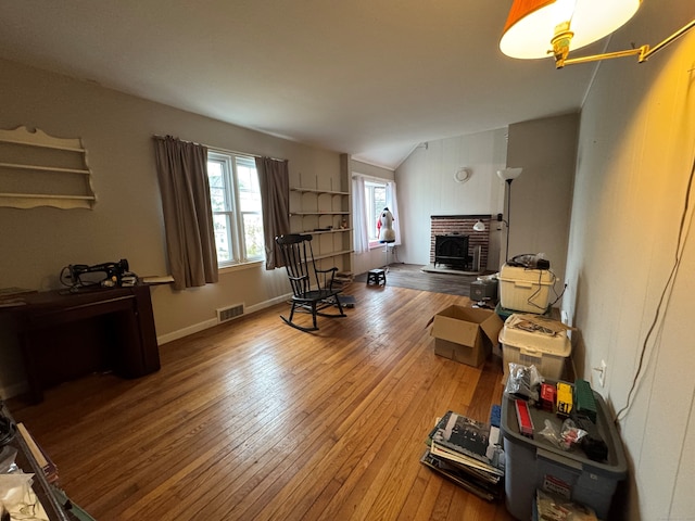 living room featuring visible vents, hardwood / wood-style floors, a fireplace, and vaulted ceiling