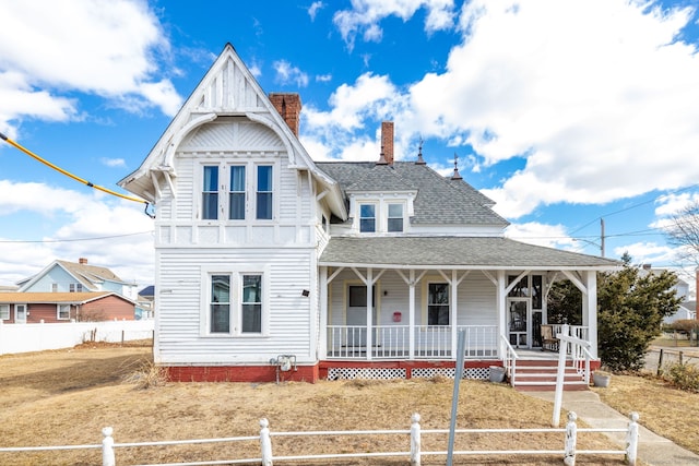 victorian home with a fenced front yard, covered porch, a chimney, and a shingled roof