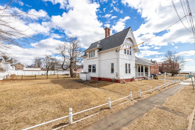 view of side of home with a shingled roof, a porch, a fenced front yard, and a chimney