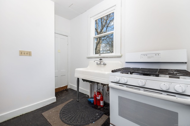 kitchen with white range with gas cooktop, baseboards, and a sink