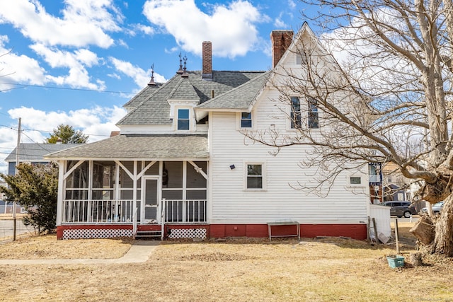 back of house featuring roof with shingles, a sunroom, and a chimney