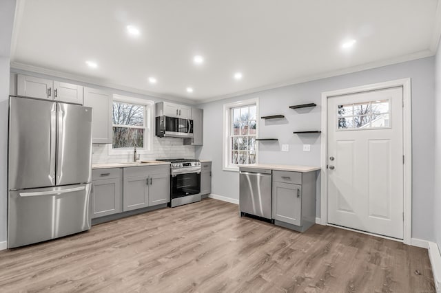 kitchen featuring gray cabinetry, appliances with stainless steel finishes, light wood-type flooring, backsplash, and crown molding