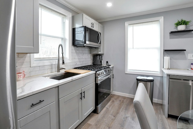 kitchen with crown molding, stainless steel appliances, decorative backsplash, a sink, and baseboards