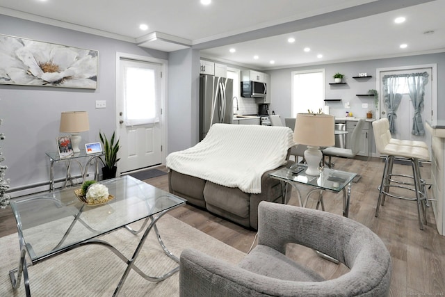 living area featuring light wood-style floors, ornamental molding, baseboard heating, and recessed lighting