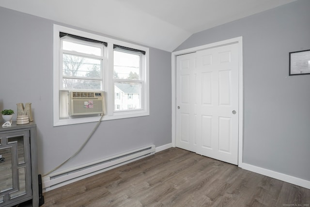 unfurnished bedroom with a baseboard radiator, wood finished floors, baseboards, vaulted ceiling, and a closet