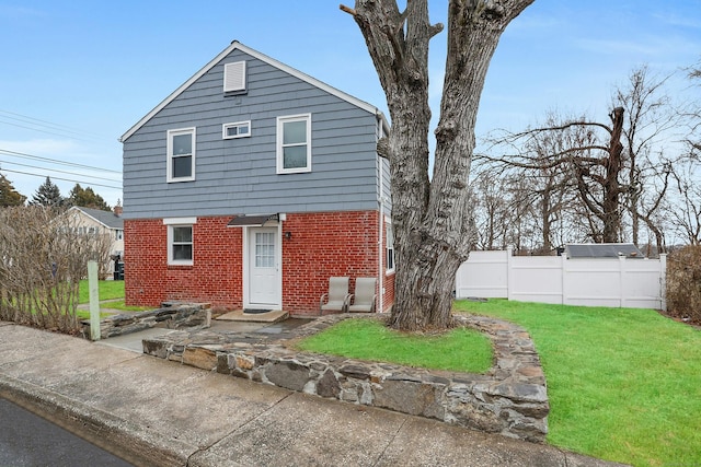 exterior space featuring brick siding, fence, and a front lawn