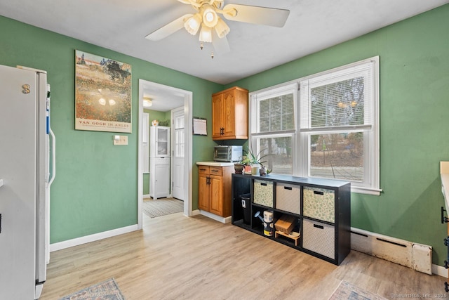 kitchen featuring a baseboard radiator, light wood-style flooring, baseboards, freestanding refrigerator, and brown cabinets