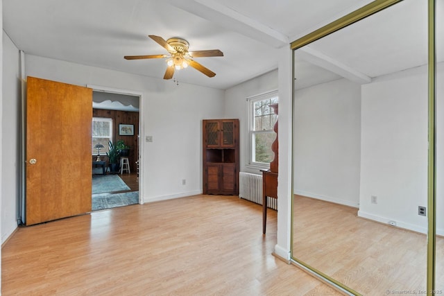 spare room featuring radiator heating unit, light wood-style floors, ceiling fan, beamed ceiling, and baseboards